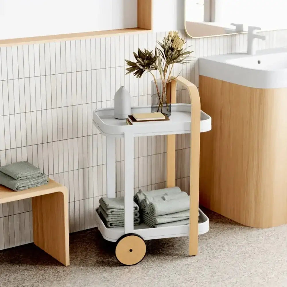Bathroom setting with a trolley holding towels and a vase of flowers, against a tiled wall.