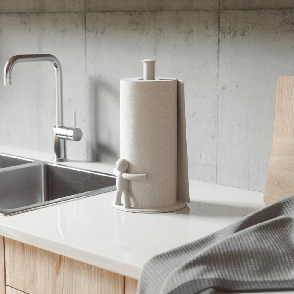 A roll of paper towels in a kitchen setting, mounted on a counter with a sink and faucet visible in the background.