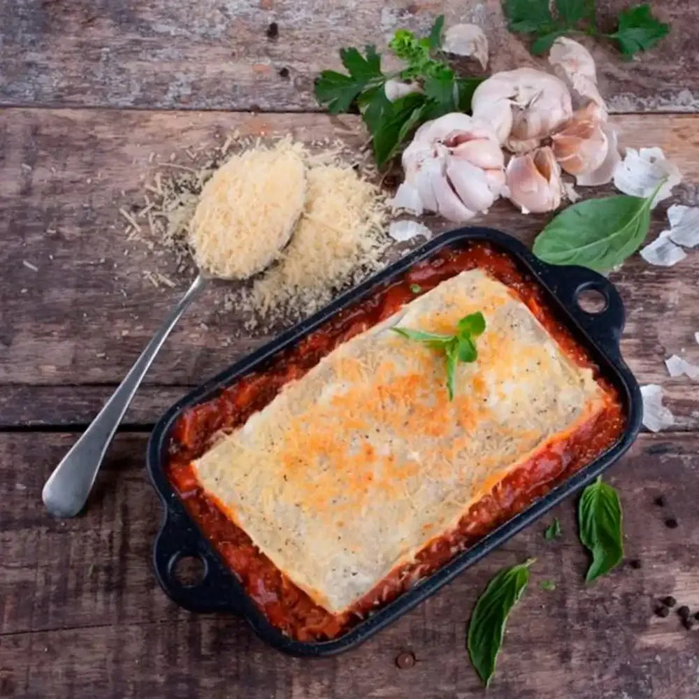 Baked dish in a pan on a wooden surface with herbs and cheese.