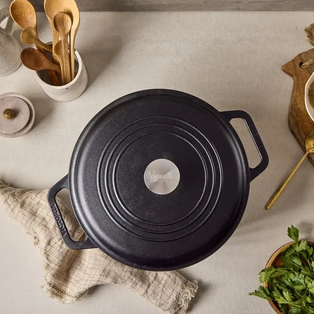 Black cast iron pot on a kitchen counter with wooden utensils and herbs.