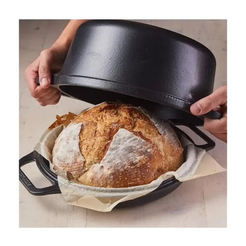 Black bread proofing basket with a loaf of bread inside on a light background