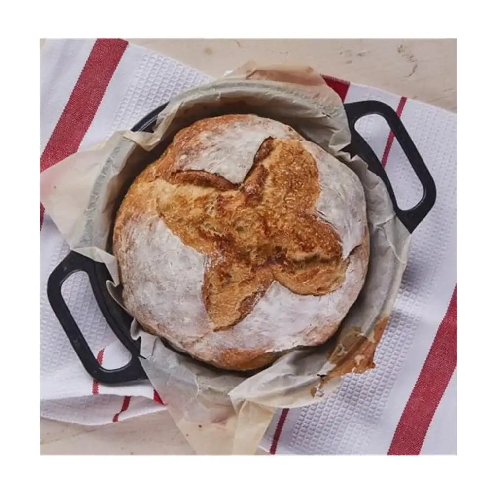 Loaf of bread in a black cast iron skillet on a red and white striped towel