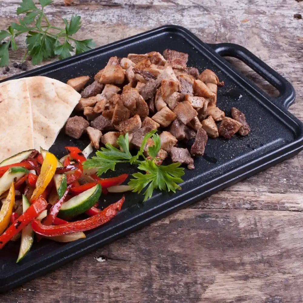 Platter of grilled meat, vegetables, and pita bread on a wooden surface