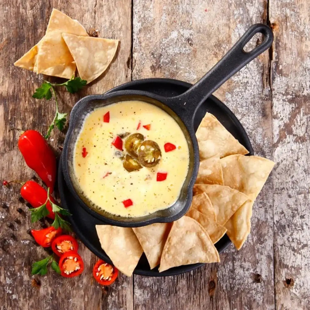 Queso dip with jalapeños and tortilla chips in a cast iron skillet on a wooden surface.