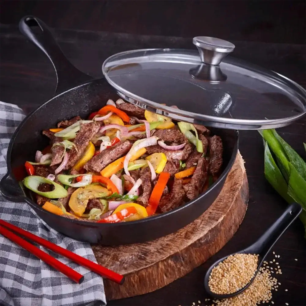 Frying pan with stir-fry vegetables and meat on a wooden board with a glass lid.