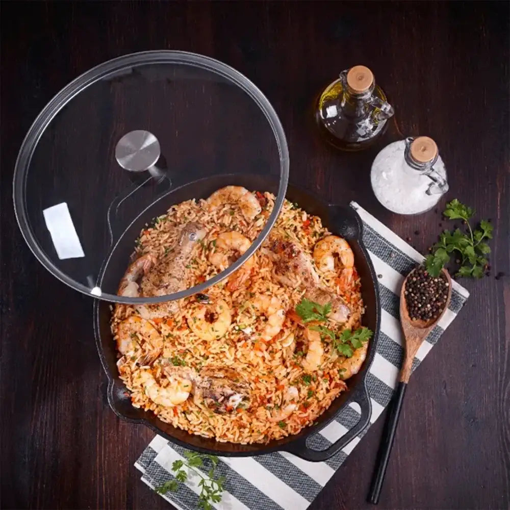 Fried rice dish with shrimp in a pan on a wooden table, surrounded by ingredients and a glass lid.
