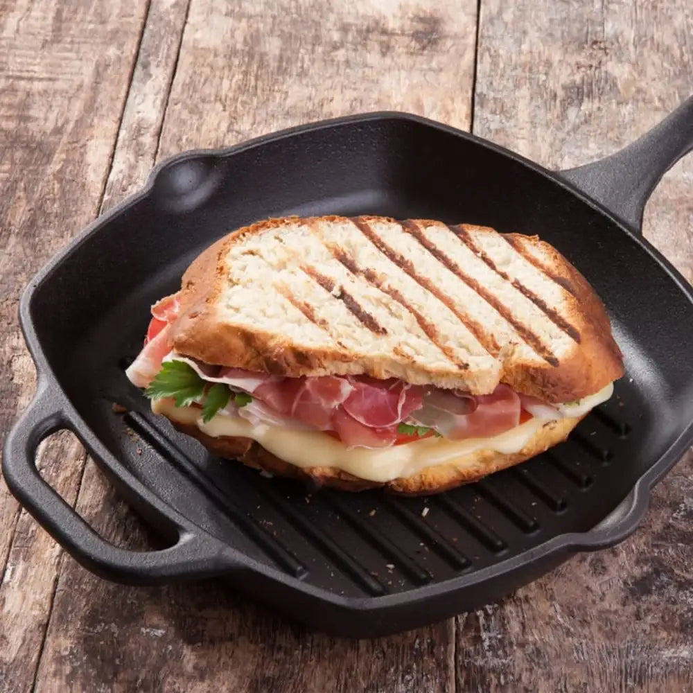 Grilled sandwich with prosciutto and cheese in a black cast iron skillet on a wooden surface