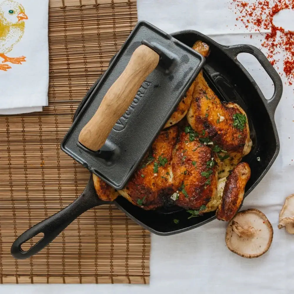 Roasted chicken in a cast iron skillet with a wooden handle on a white surface.