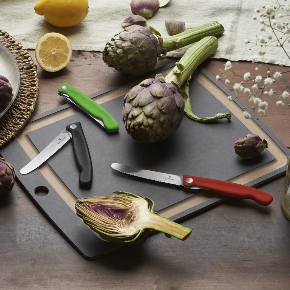 Artichokes on a cutting board with knives and lemons on a wooden surface