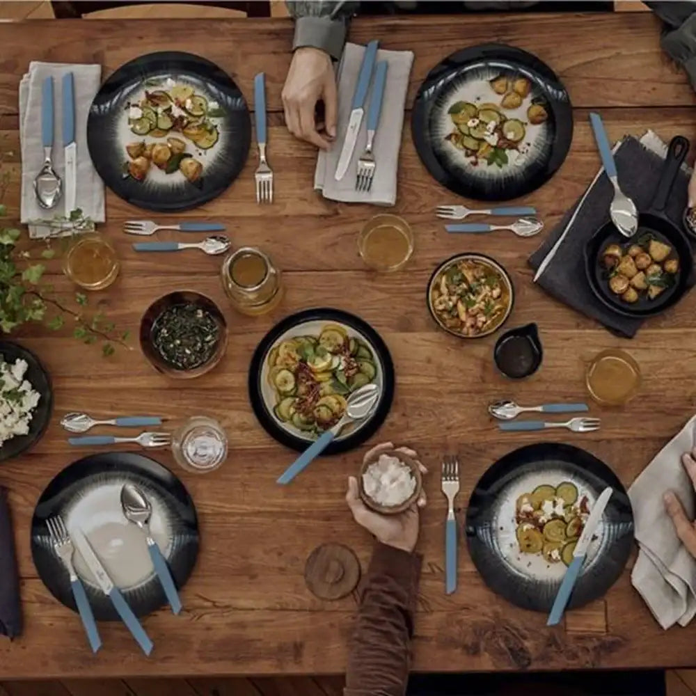 Dining table set with plates of food, cutlery, and drinks on a wooden surface.