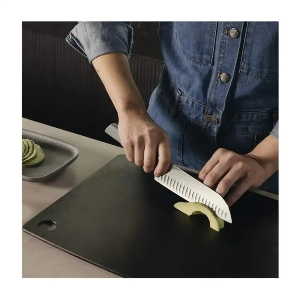 Person cutting avocado on a black cutting board with a knife