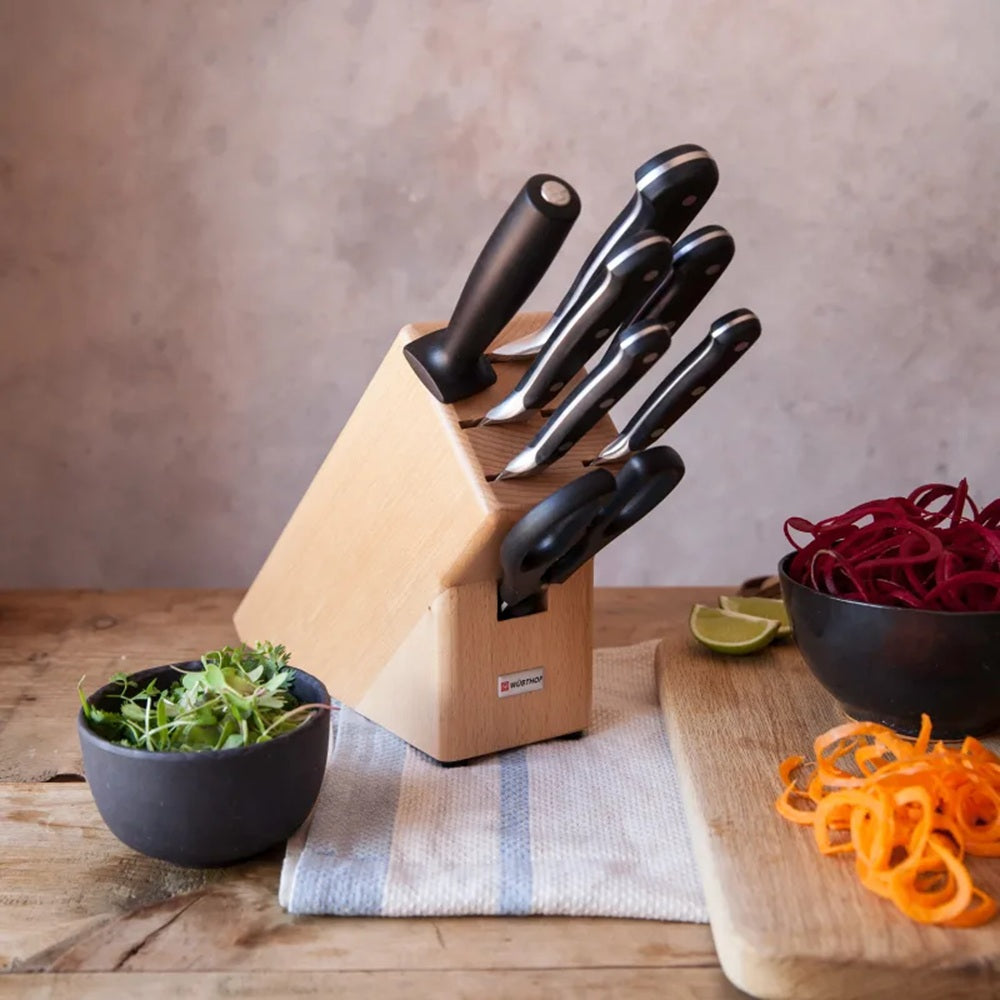 Set of knives in a wooden block on a kitchen counter with vegetables.