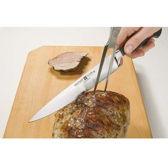 Knife and fork cutting into a piece of meat on a wooden board with a white background