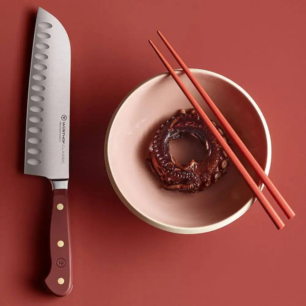 Knife with a red handle next to a bowl of food and chopsticks on a red background