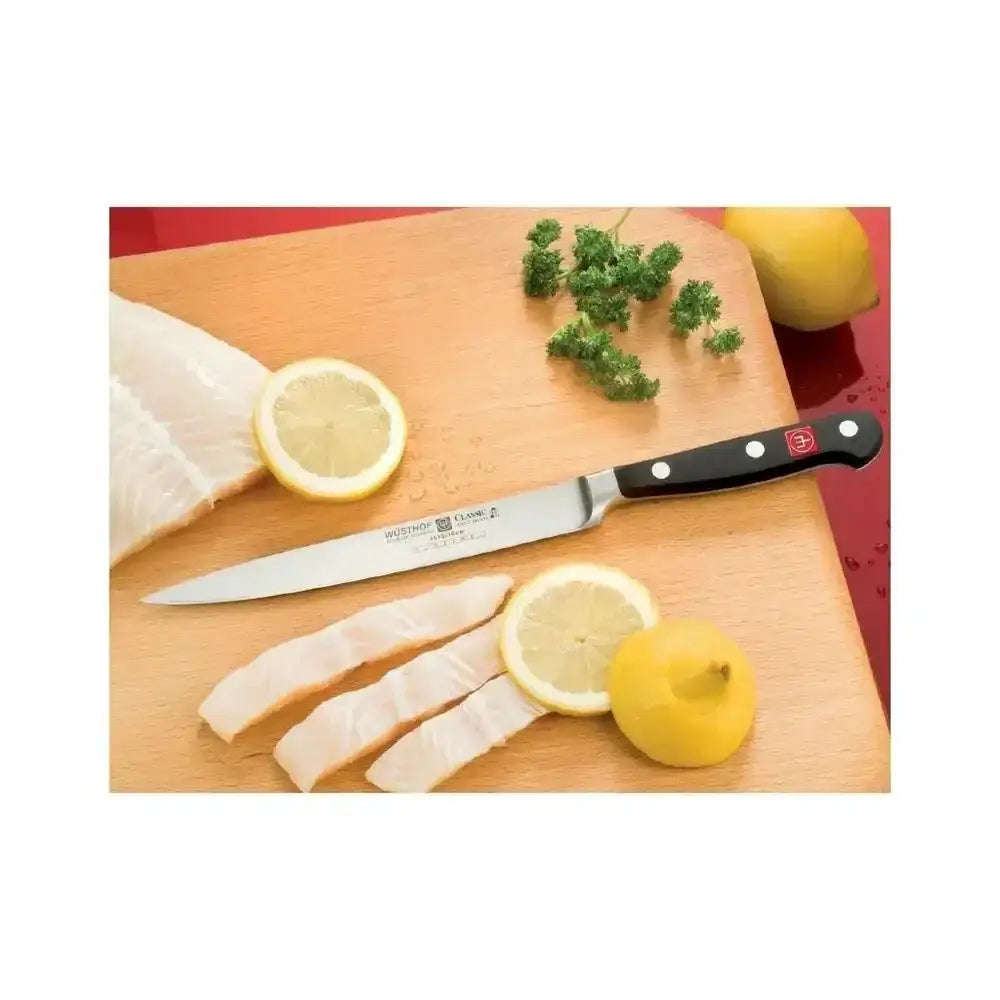 Knife on a wooden cutting board with fish fillets, lemons, and herbs.