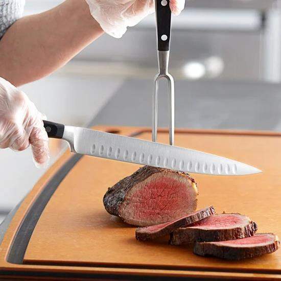 Person cutting a steak on a wooden board with a knife and fork, wearing gloves.