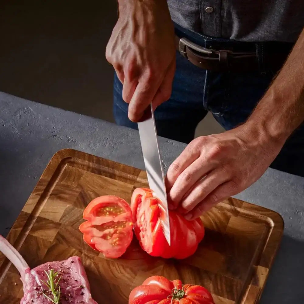 Person cutting a tomato on a wooden cutting board with a knife.