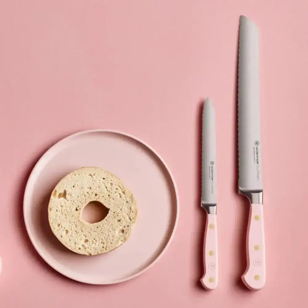 Bagel on a pink plate with two knives on a pink background