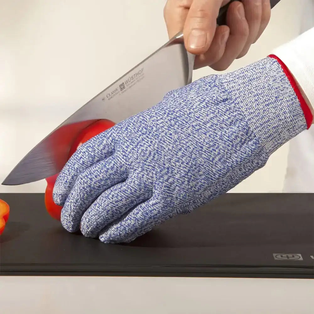 Person wearing a blue cut-resistant glove cutting a red tomato with a knife on a black cutting board.