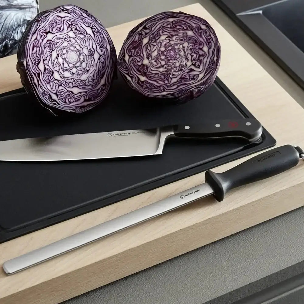 Two halves of a purple cabbage on a cutting board with a knife and another tool.