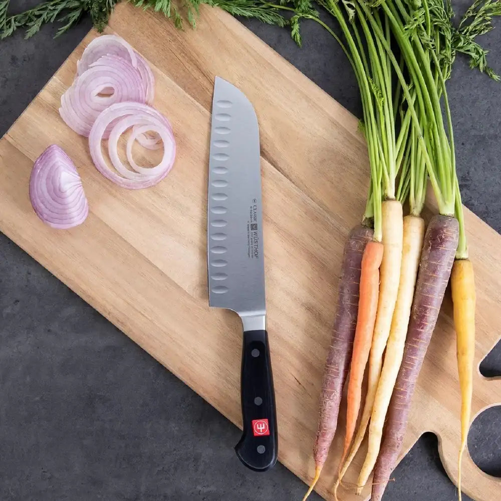 Colorful carrots, sliced onions, and a knife on a wooden cutting board.