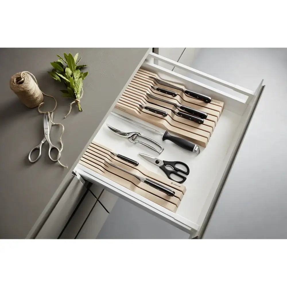 Set of knives and scissors in a drawer with a roll of twine and leaves on a gray surface.