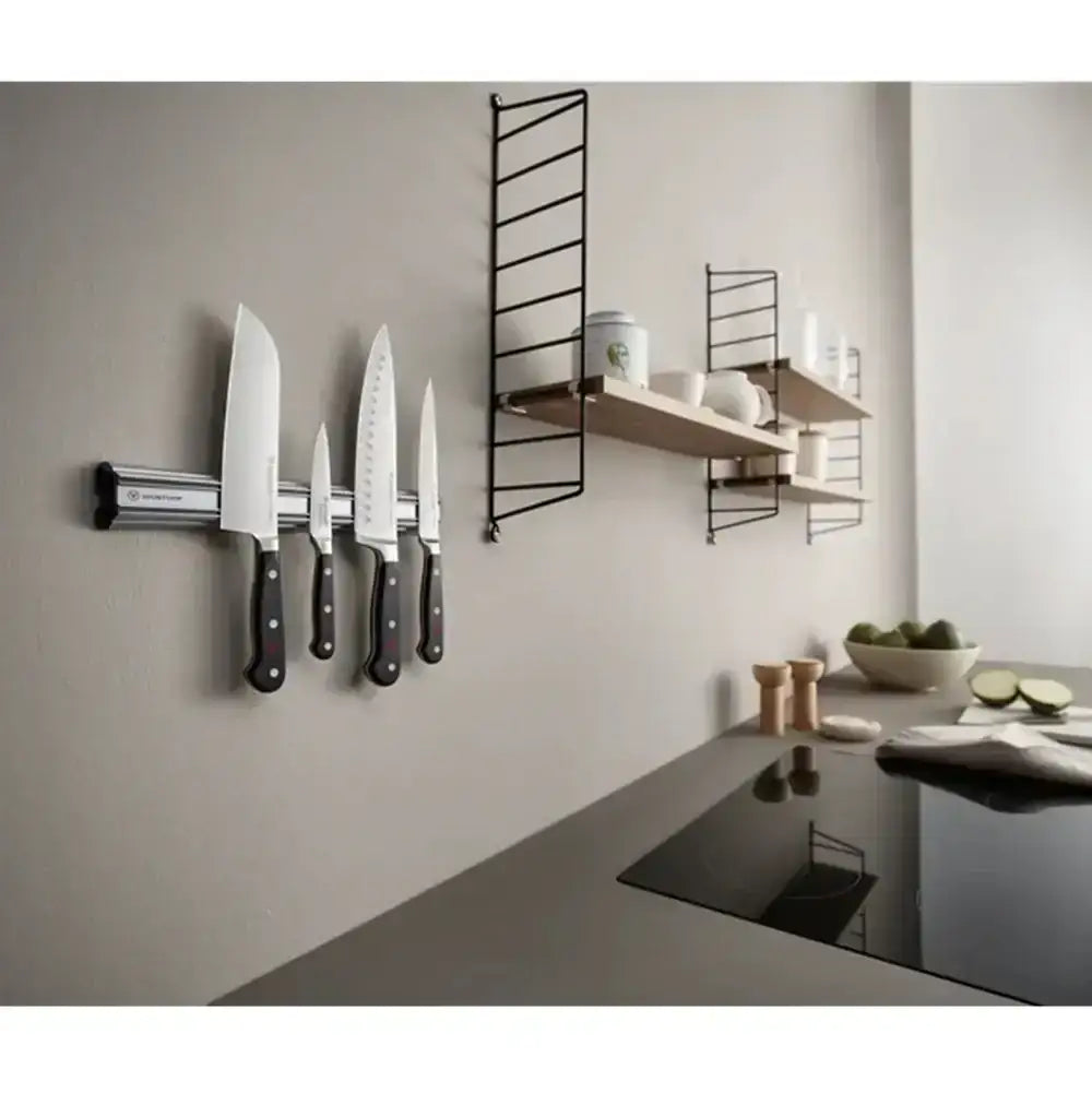 Kitchen setting with knives on a magnetic wall strip and shelves above a stove.