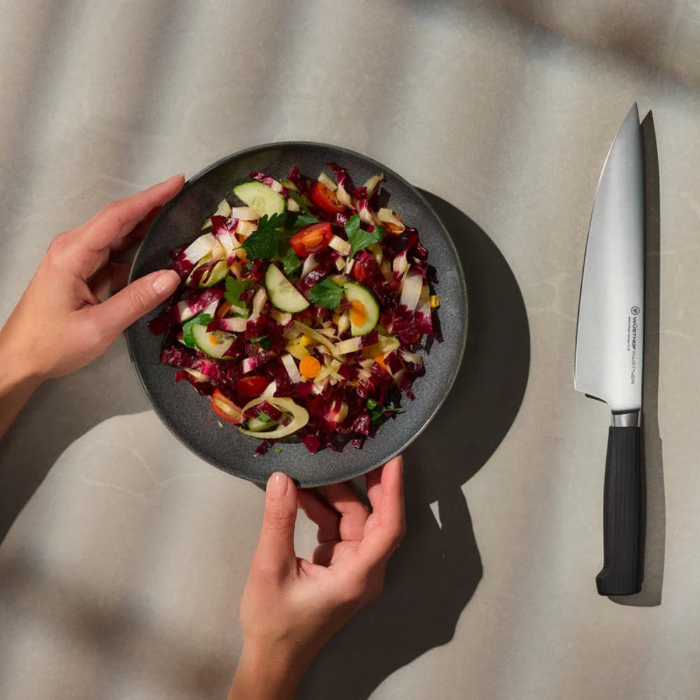Person holding a plate of salad with a knife and radicchio on a neutral background