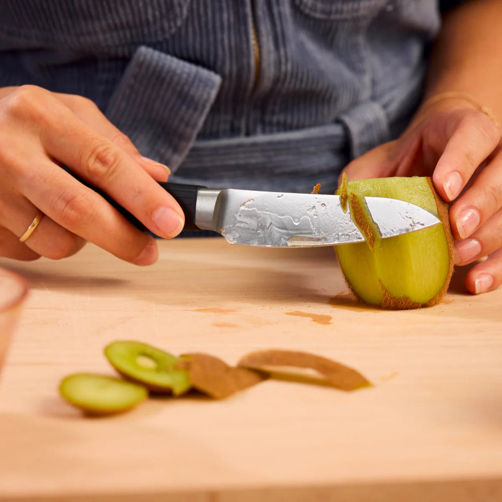 Person cutting a kiwi fruit on a wooden cutting board with a knife.