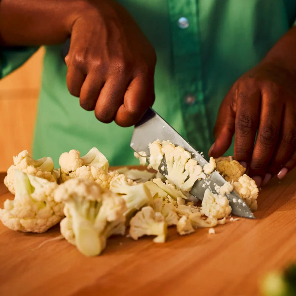 Person cutting cauliflower on a wooden cutting board with a knife.