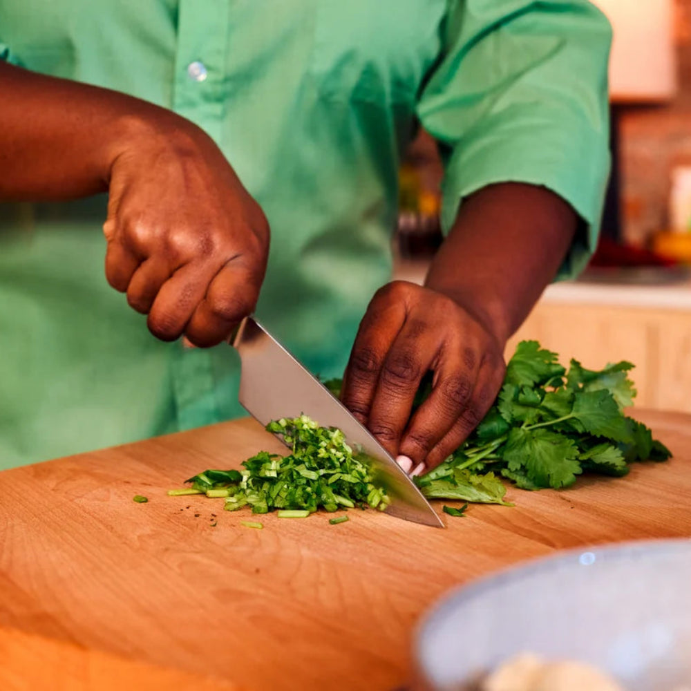 Person chopping greens on a wooden cutting board with a knife