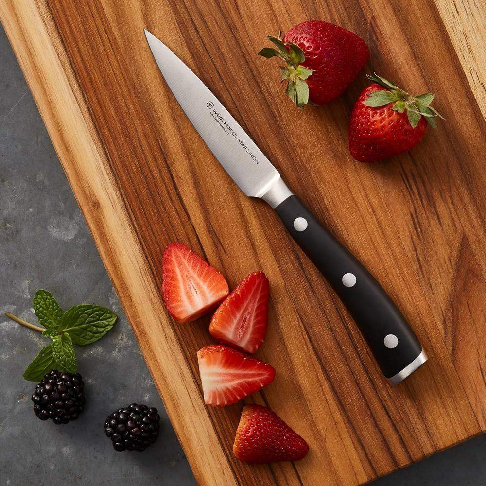 Paring knife on a wooden cutting board with sliced strawberries and blackberries.