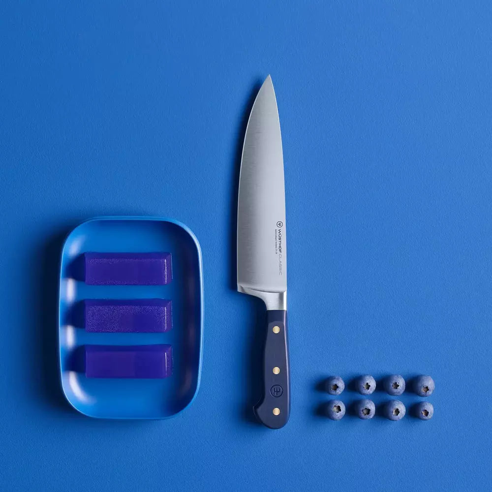 Knife with a blue handle on a blue background, next to a blue tray with purple items and blueberries.