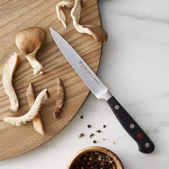Knife on a wooden cutting board with mushrooms and peppercorns on a marble surface