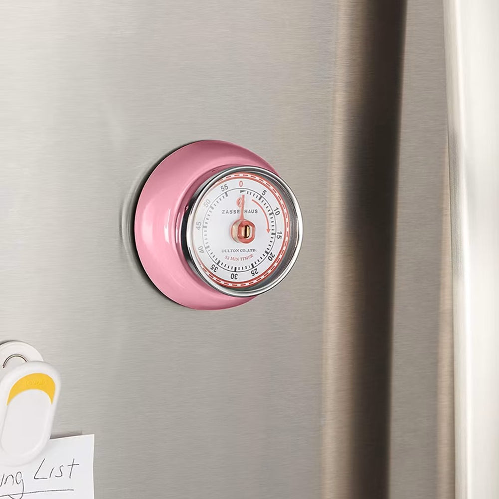 A pink round kitchen timer with a clear face and silver rim, attached to a brushed stainless steel refrigerator door.