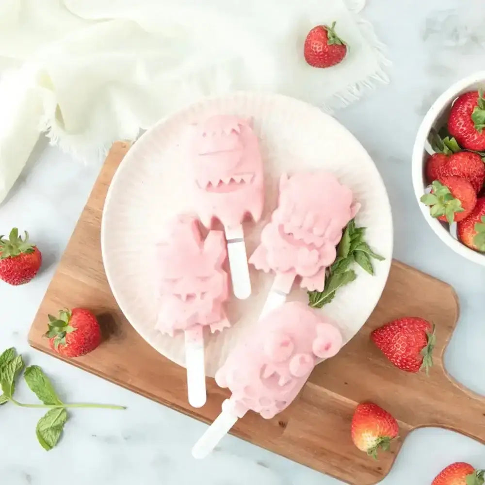 Pink ice cream popsicles on a white plate with strawberries around
