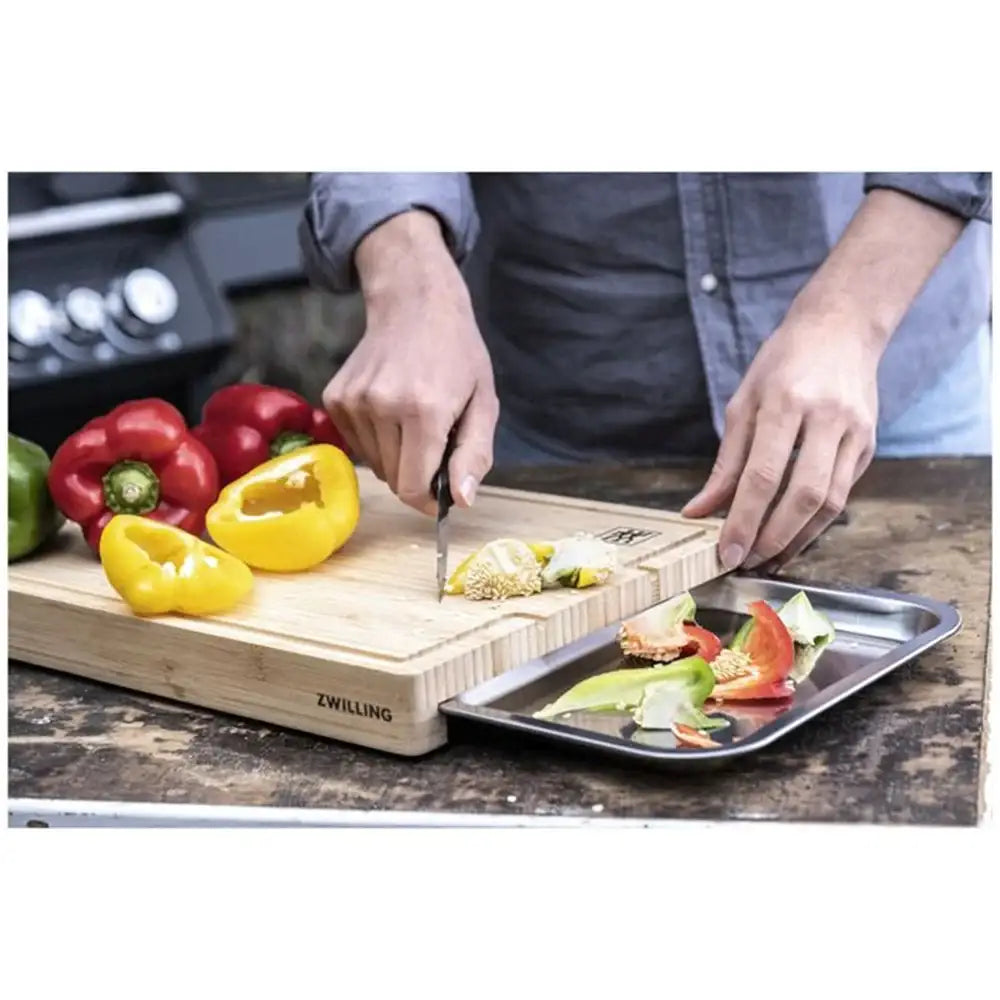 Person cutting vegetables on a wooden cutting board with a knife, surrounded by colorful peppers.