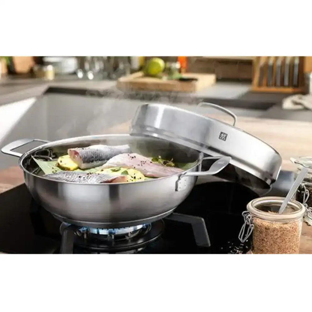Stainless steel wok with lid on a stove, cooking fish and vegetables.