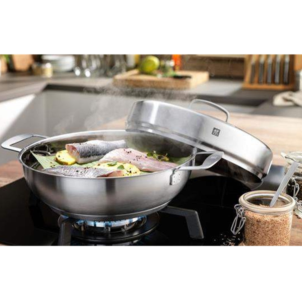 Stainless steel wok with lid on a stove, cooking fish and vegetables.