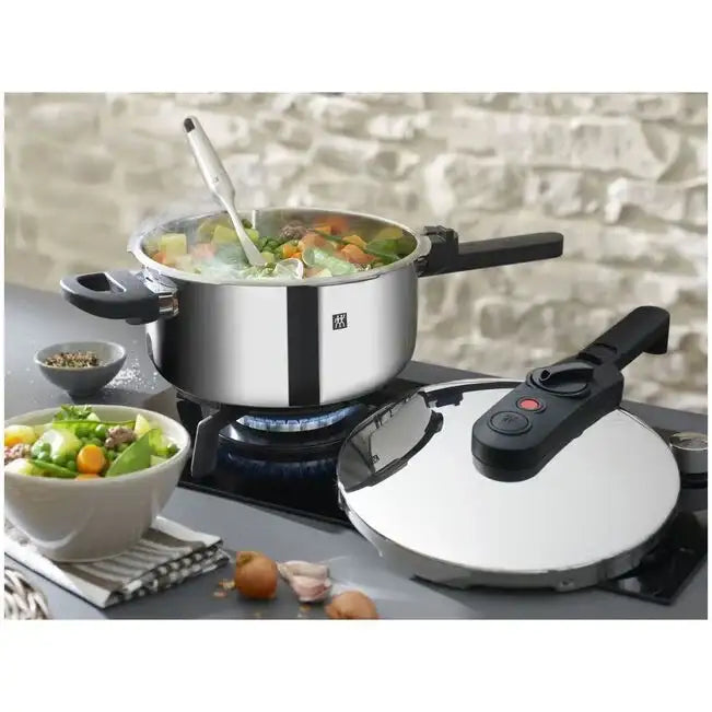 Stainless steel pot with food on a gas stove, next to a pressure cooker and bowls of salad.