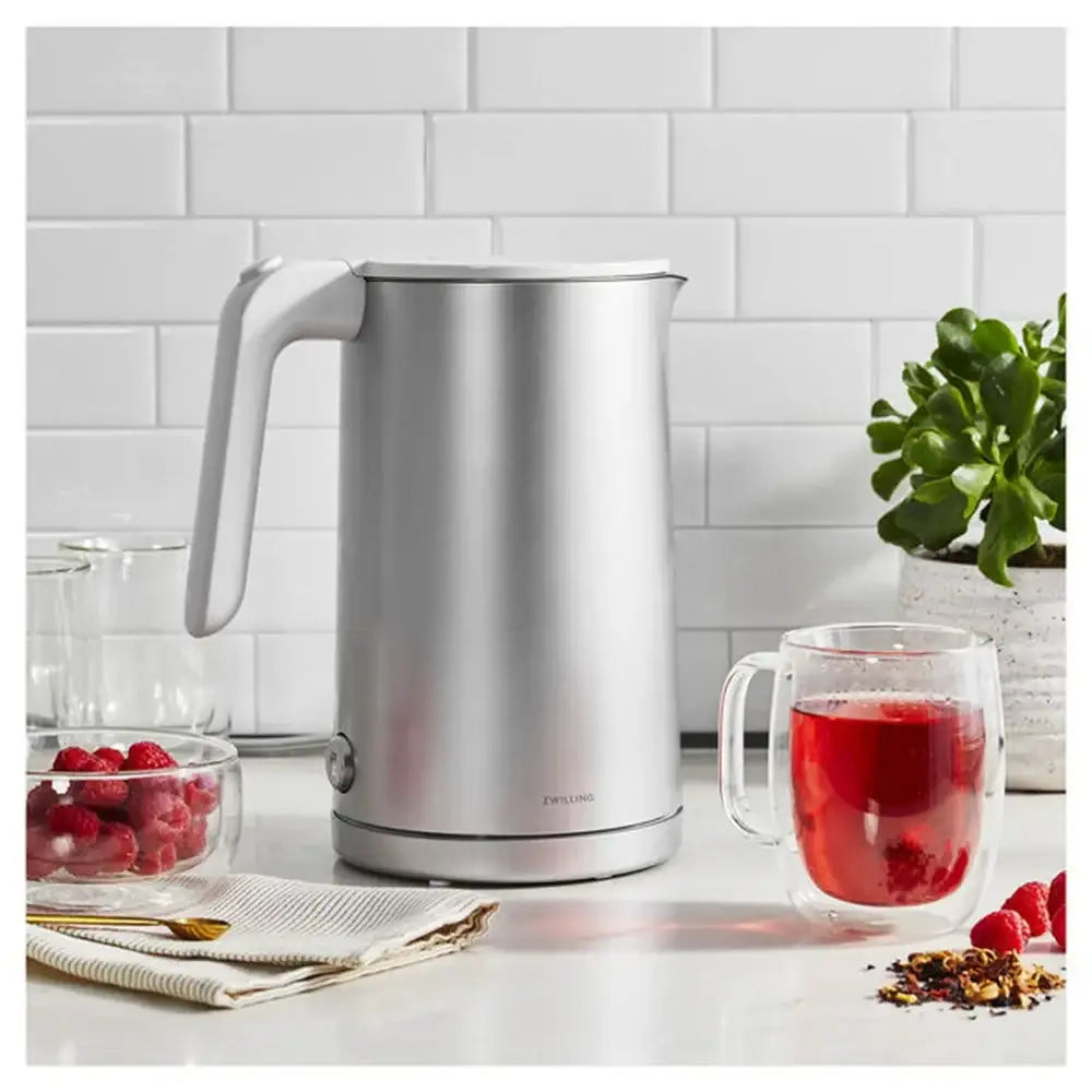 Silver electric kettle on a kitchen counter with a glass of red tea and berries.