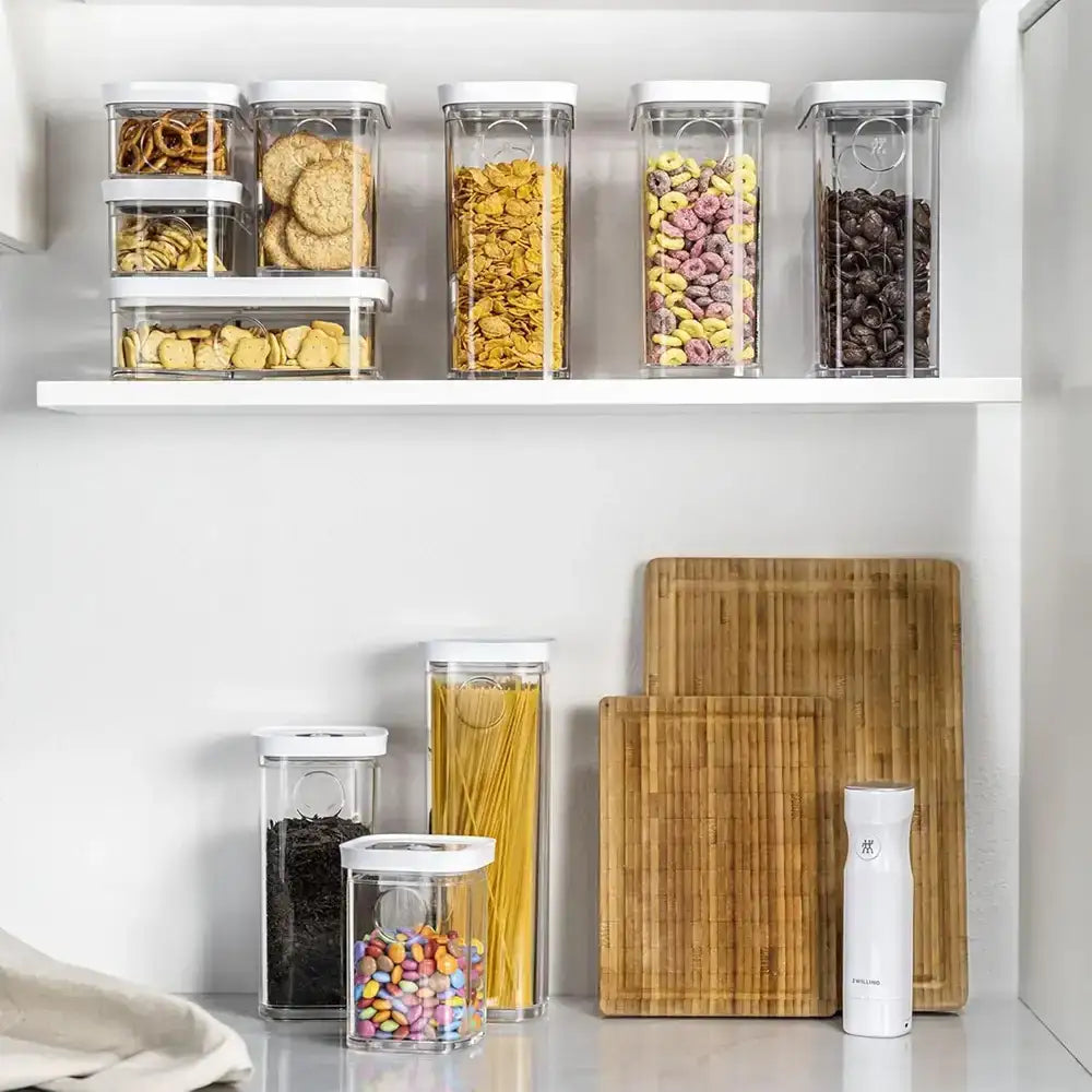 Clear storage containers with food on a kitchen shelf, next to wooden cutting boards and a white container.