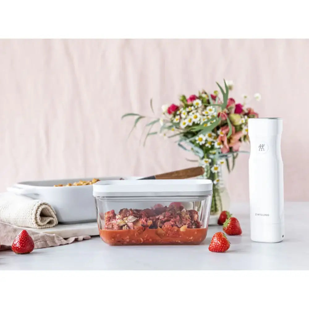 Glass food container with strawberries on a table with a pink background