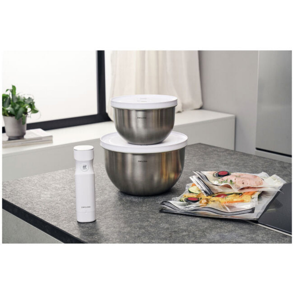 Two stainless steel mixing bowls on a kitchen counter with a white container next to them.