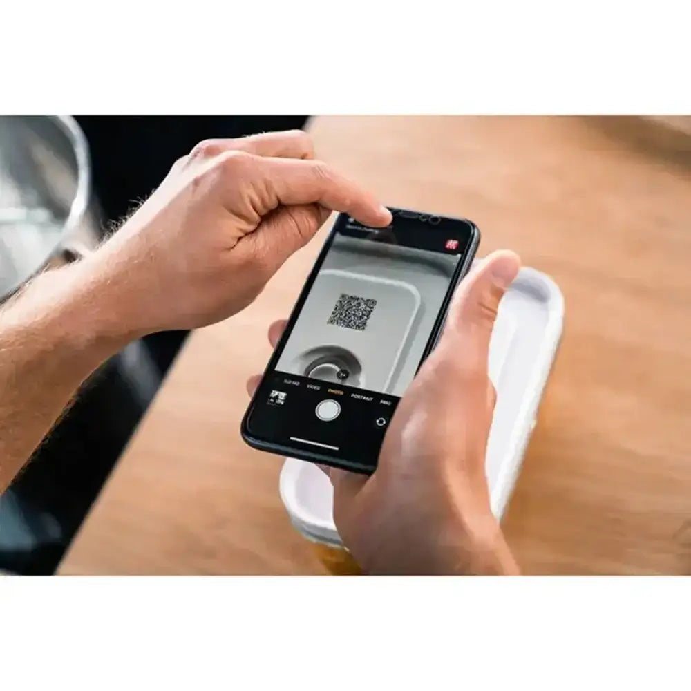 Person using a smartphone to scan a QR code on a white container.