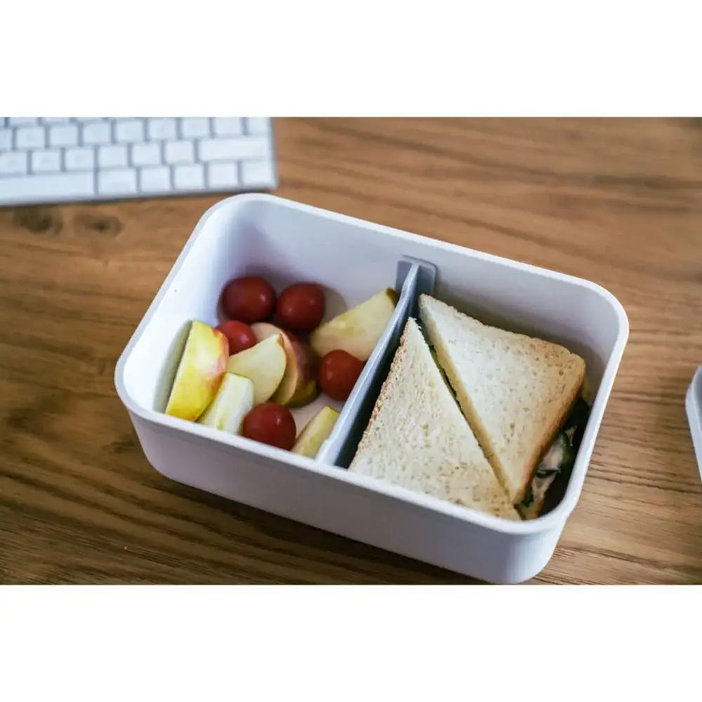 Lunch container with a sandwich and fruits on a wooden desk