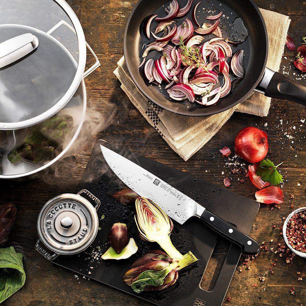 Cooking scene with a frying pan, knife, and vegetables on a wooden surface.