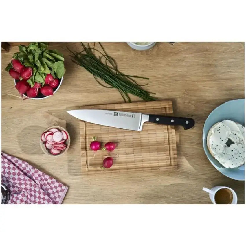 Knife on a wooden cutting board with radishes and other vegetables on a wooden table.