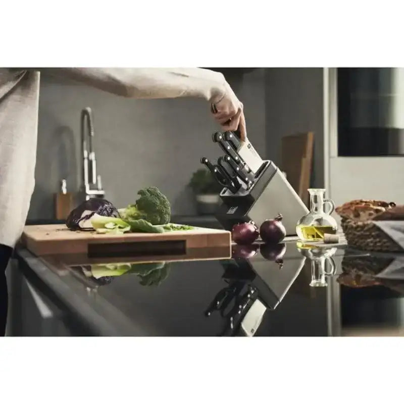 Person using a knife block with kitchen utensils on a counter.