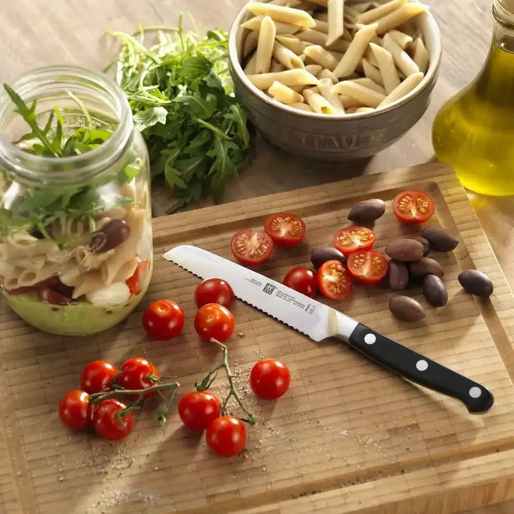 Wooden cutting board with ingredients for a pasta salad including tomatoes, olives, and a jar of salad.